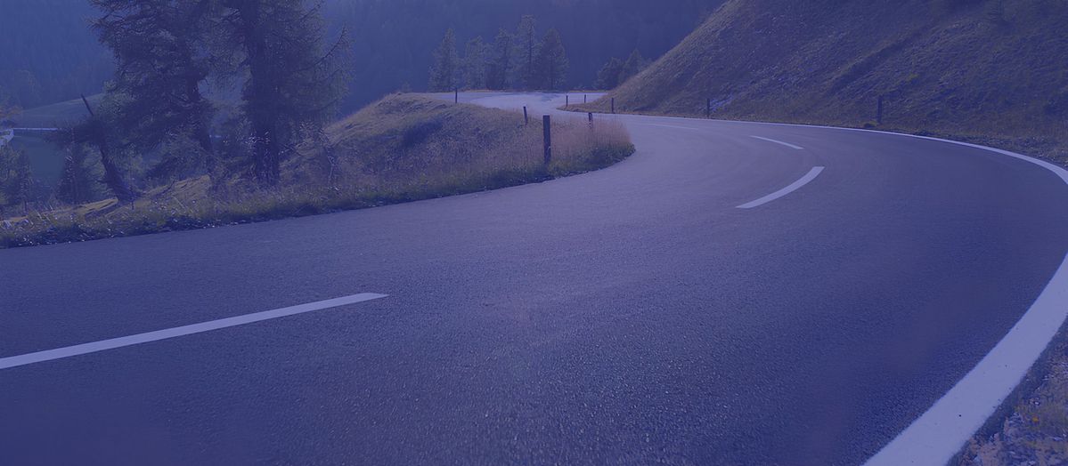 Kurvige Bergstraße mit weißer Fahrbahnmarkierung und grasbewachsenen Hängen im Hintergrund